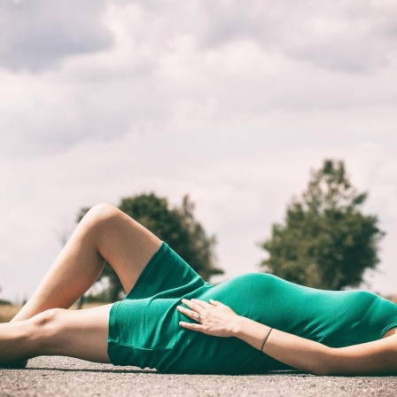 Eine schwangere Frau liegt auf dem Boden in einem grünen Kleid.
