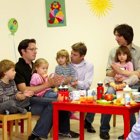 Väter sitzen mit ihren Kindern an einem Kindertisch in einer Krabbelgruppe