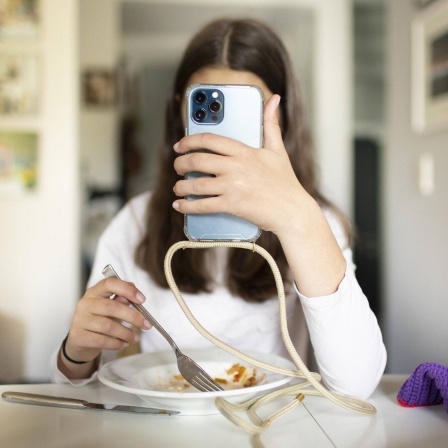 Das Beitragsbild des Dok5 "Gefährliche Freundschaften - Im Hungern nicht allein" zeigt ein Mädchen vor einem Teller Nudeln, die ihr Smartphone vor ihr Gesicht hält. 