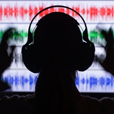 Eine Frau sitzt mit Kopfhörern vor einem Monitor, auf dem verschiedene Tonspuren angezeigt werden (Bild: picture alliance/dpa | Jens Büttner)
