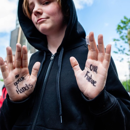 Ein junger Demonstrant der Gruppe Extinction Rebellion zeigt seine Hände, auf denen geschrieben steht: "In your Hands - Our Future", zu Deutsch: "In deinen Händen - unsere Zukunft"