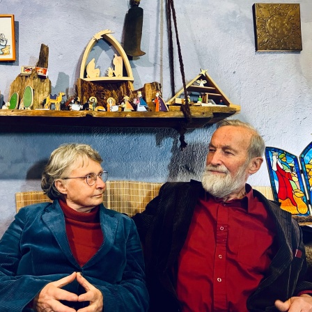 Eine ältere Dame und ein älterer Heer sitzen inmitten von Weihnachtsschmuck und schauen sich an.