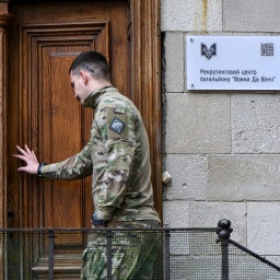 Ein Mann in Flecktarn-Bekleidung öffnet die hölzerne Tür eines Rekrutierungsbüros in Lwiw.
