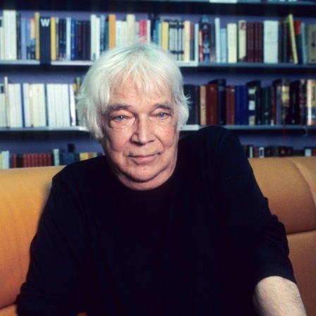 Das Beitragsbild des Kulturfeature Thomas Harlan und seine Erkundungen zum „Vierten Reich“ zeigt Thomas Harlan 2020 vor einer Bücherwand