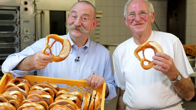 Horst Lichter und ein Bäcker halten in einer Backstube jeweils eine Brezel in der Hand