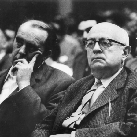 Adorno und Böll sitzen in einem Hörsaal und schauen nach vorn.