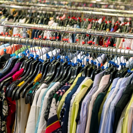 Textilien als Massenware: Verschiedenfarbige Hemden, Blusen und Westen werden im Einzelhandel als Massenware auf endlosen Kleiderstangen angeboten.