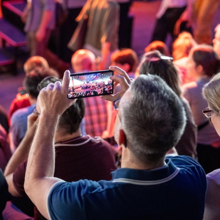 Ein Mann steht im Publikum der re:publica und macht mit seinem Smartphone ein Foto von der Bühne.