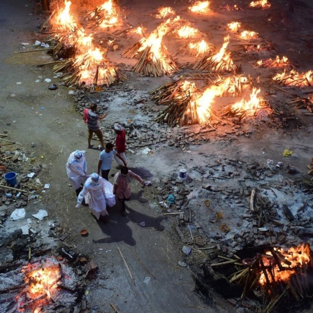 Das Foto zeigt Arbeiter in Schutzanzügen und Familienmitglieder, die in Neu-Delhi am 1. Mai 2021 einen Leichnam zur Einäscherung inmitten mehrerer Scheiterhaufen auf ein Gelände tragen, das in ein Krematorium für Masseneinäscherungen umgewandelt wurd