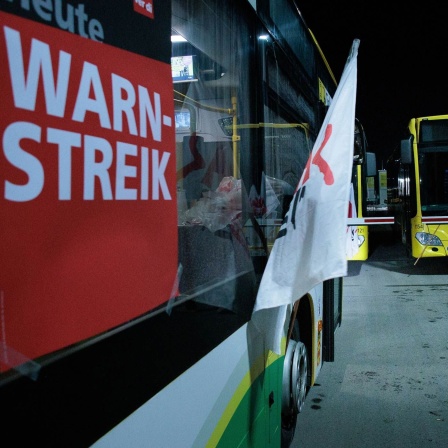 Eine Frau geht an Bussen der Berliner Verkehrsbetriebe BVG mit Fahnen der Gewerkschaft Verdi und dem Schild "Heute Warnstreik" im Betriebshof Lichtenberg entlang (Bild: picture alliance/dpa/Carsten Koall)