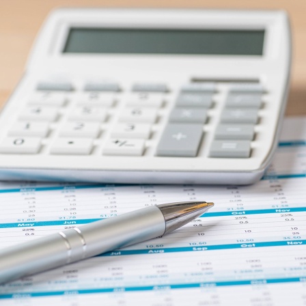 Ein Taschenrechner, Stift, Ordner und ein Blatt Papier auf einem Holztisch