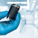 Eine Hand mit blauem Hanschuh biegt eine flexible Solarzelle der Empa