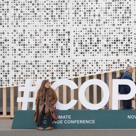 Eine Teilnehmerin sitzt vor dem Logo der COP29 in Baku. 