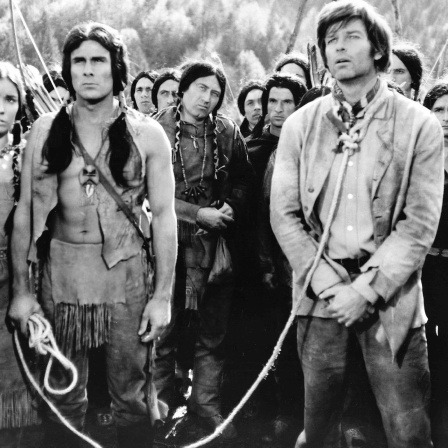 Ein Cowboy an einer Leine steht vor eine Gruppe Indigener, einer von diesen hält das Ende der Leine.