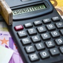 Haus auf Geldscheinen und Taschenrechner mit dem Schriftzug Grundsteuer