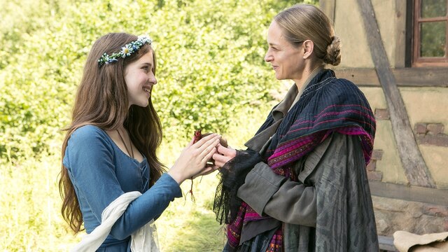 Tränenreicher Abschied von der Waldfrau. Die Waldfrau (Sophie von Kessel, re.) überreicht Prinzessin Amélie (Leonie Brill) ein Säckchen mit Salz für ihren Vater.