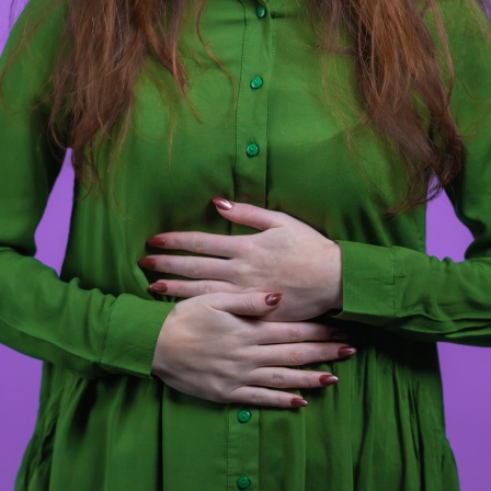 Eine Frau in Bluse hält sich mit beiden Händen den Bauch