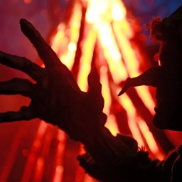 Im Hexenkostüm steht ein Besucher des Walpurgisfestes in Schierke am Feuer.