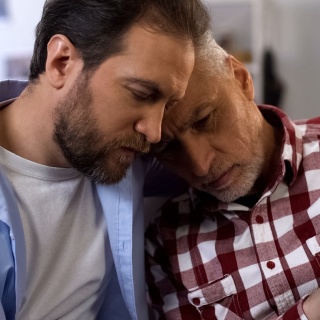 Junger Mann umarmt und tröstet depressiven alten Mann.