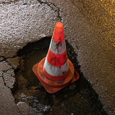 Ein orange-weiß gestreifter Verkehrs-Pylon steht in einem tiefen Schlagloch in einer Berliner Straße