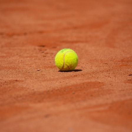 Ein gelber Tennisball liegt auf einem roten Ascheplatz