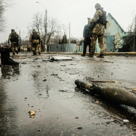 Ukrainische Soldaten inspizieren die Trümmer einer zerstörten russischen Panzerkolonne auf einer Straße in Butscha.