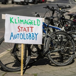 An Fahrräder gelehnt steht ein Protestplakat mit der Aufschrift: "Klimageld statt Autolobby".