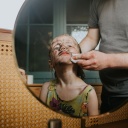 Blick in den Spiegel. Darin zu sehen ist ein Kind mit schmutzigem Gesicht und schelmischem Ausdruck. Eine Person schrubbt dem Kind mit einem Lappen das Gesicht.