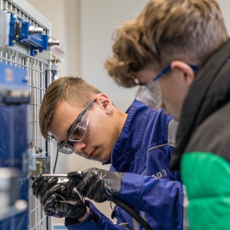Ein Mechantroniker im dritten Ausbildungsjahr zeigt im Hydraulikkabinett an einer Versuchswand Aufgaben aus seiner Ausbildung.