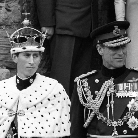 Prinz Charles mit Krone und Umhang nach seiner Ernennung 1969. Neben ihm steht Prinz Philip in Uniform. Schwarz-weiß-Bild.