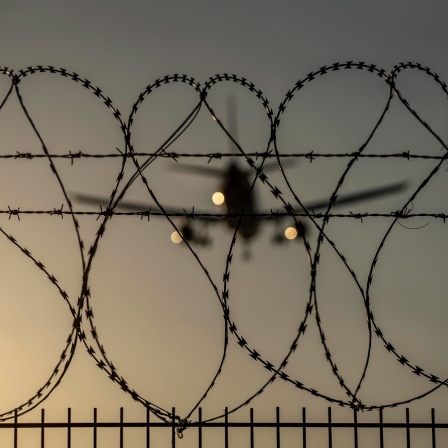 Ein Stacheldrahtzaun am Flughafen Düsseldorf - mit einem Flugzeug im Hintergrund. 