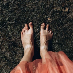 Blick auf nackte Frauenfüße im Gras, dunkel gehaltenes Bild.