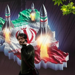 Ein Passant, der mit einem Handy telefoniert, geht an einem Banner vorbei, das den Abschuss von Raketen von der iranischen Landkarte im Norden Teherans zeigt.