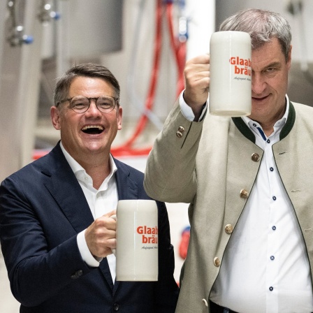 Markus Söder (CSU), Ministerpräsident von Bayern, und Boris Rhein (CDU), Ministerpräsident von Hessen, halten bei der Besichtigung der Brauerei Glaabsbräu in Seligenstadt Bierkrüge in den Händen.