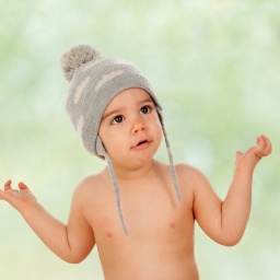 Ein nur mit Mütze bekleidetes Kleinkind hebt fragend die Arme.