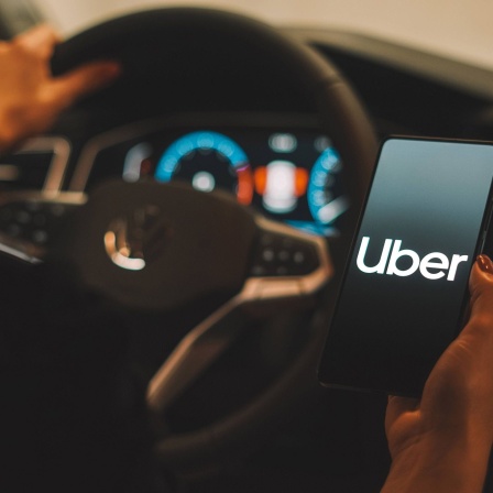 Symbolbild:Eine Fahrerin hält ein Handy mit einer Anzeige der App Uber in der Hand.