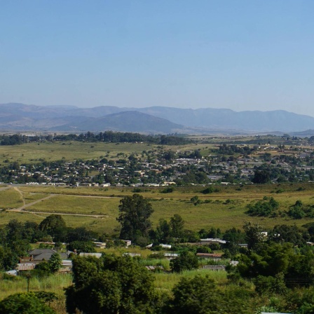 Blick auf Landschaft und Lubombo-Berge im Königreich Eswatini. Eine große grüne Fläche, im Hintergrund sind Berge und ein heller blauer Himmel zu sehen. 