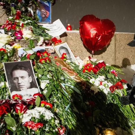 Jemand legt Blumen an einem Gedenkort mit dem Foto des gestorbenen russischen Oppositionellen Nawalny nieder