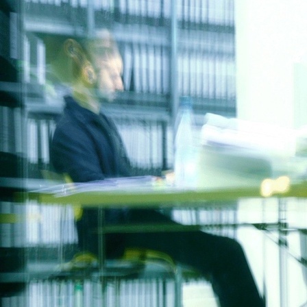 Ein Mann sitzt abends in einem Büro an einem vollen Schreibtisch und arbeitet in Berlin. 