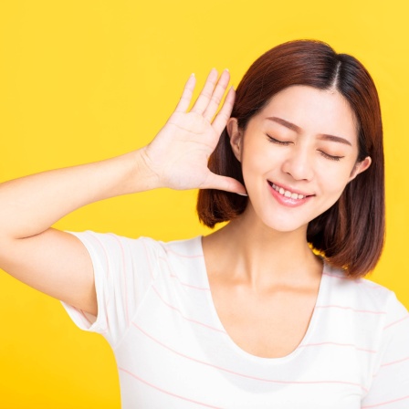 Junge Frau hält sich lauschend eine Hand hinter das Ohr: Absolutes Gehör bedeutet, dass ich zu jemandem sagen kann &#034;Sing mal ein G!&#034; - und die Person trifft dann genau den richtigen Ton. Das ist eine besondere musikalische Gabe.