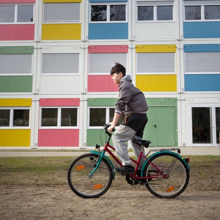 Ein Junge fährt mit einem Fahrrad an Wohncontainern vorbei.