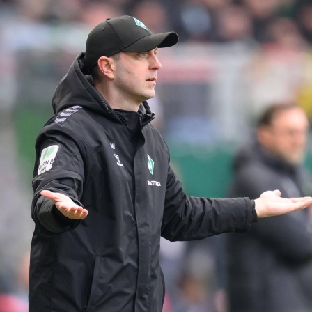 Werder-Trainer Ole Werner steht an der Seitenlinie und macht mit ausgebreiteten Armen eine fragende Geste.