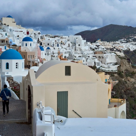 Ein Tourist nähert sich einer orthodoxen Kirche mit blauer Kuppel in Oia auf der erdbebengeschädigten Insel Santorini. 