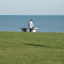 Eine Person sitzt allein auf einer Bank mit leicht gesenktem Kopf vor dem Meer.