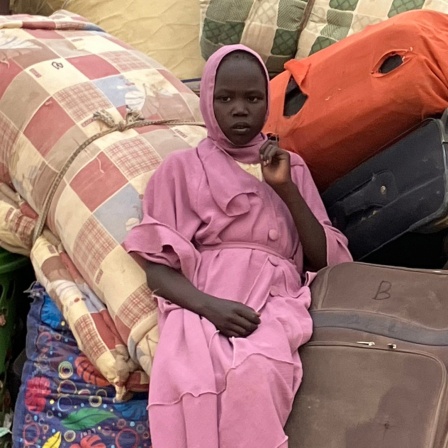 Ein Mädchen aus dem Sudan sitzt im Transitlager inmitten von Koffern, dem Hab und Gut der Flüchtlinge.