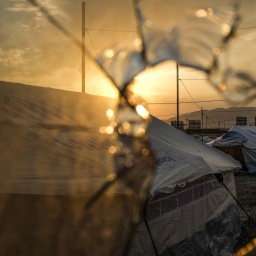Ein zerschossene Scheibe, dahinter das Flüchtlingscamp Badarash im Nordirak.