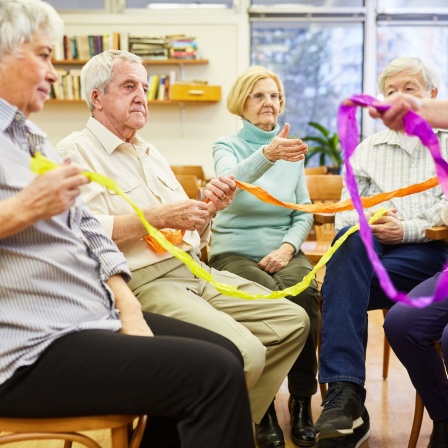 Senioren mit Demenz machen eine Übung mit bunten Stoffbändern für Interaktion