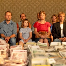 Viele Menschen sitzen vor alten Geldscheinen auf einem Tisch - Szene aus dem Kinofilm "Zwei zu eins"