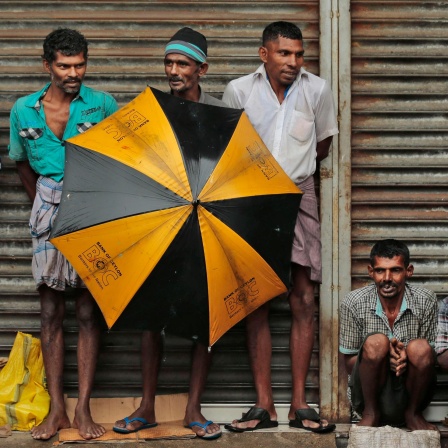 Ethnische tamilische Arbeiter aus Sri Lanka schützen sich mit Schirmen vor starkem Regen in einem Gewerbegebiet in Colombo, Sri Lanka. 