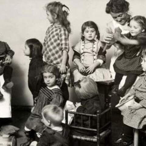 Kinder um zwei Frauen in Schwesterntracht sitzend, es wird vorgelesen